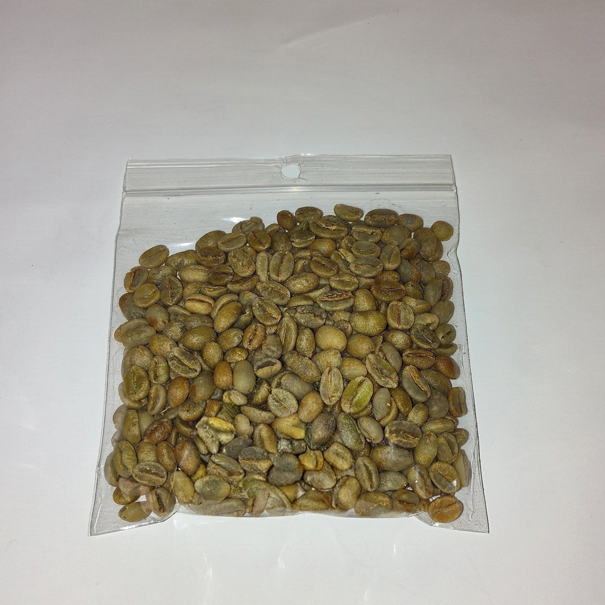 A clear plastic zip-top bag filled with green coffee beans, photographed on a plain white background.