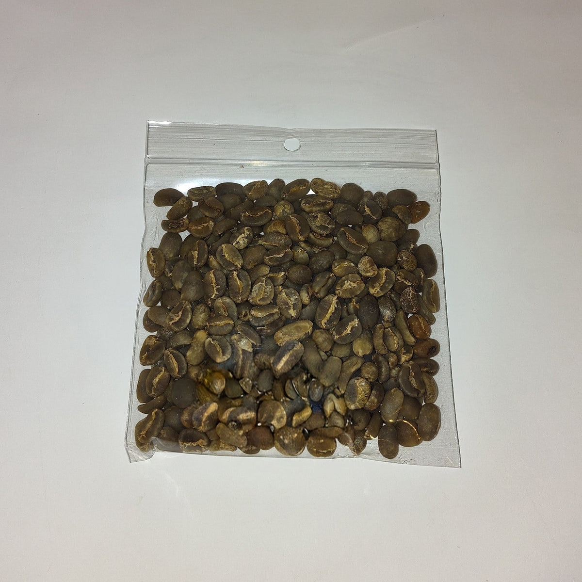 A small clear plastic zip-top bag filled with brown and tan coffee beans, photographed on a plain off-white background.
