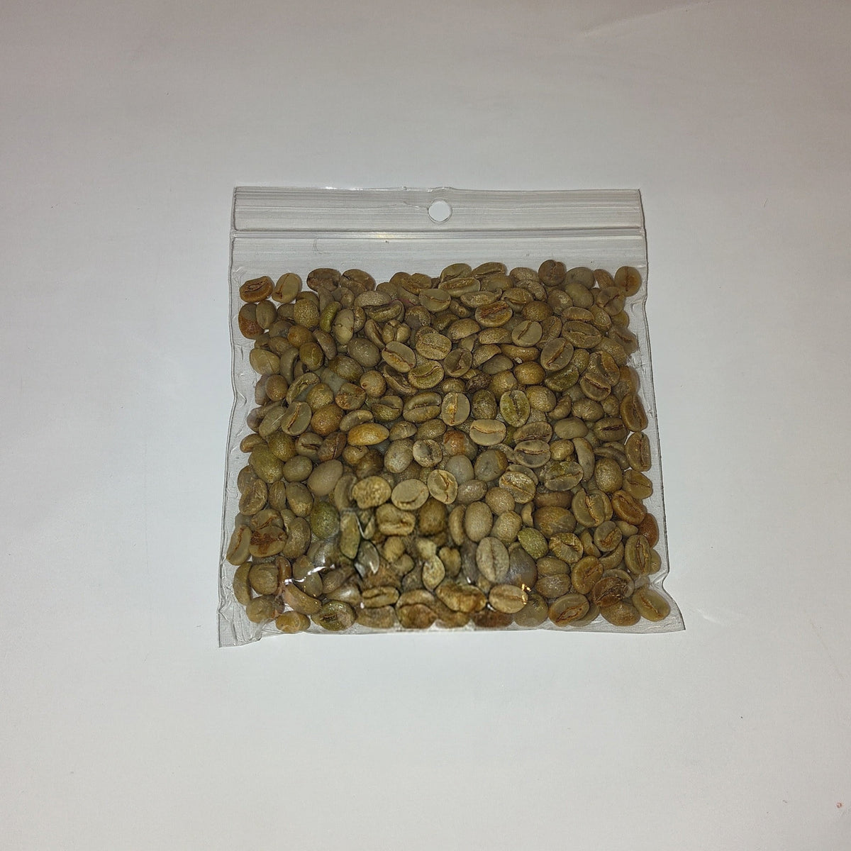 A small clear plastic zip-top bag filled with green coffee beans, photographed on a plain off-white background.